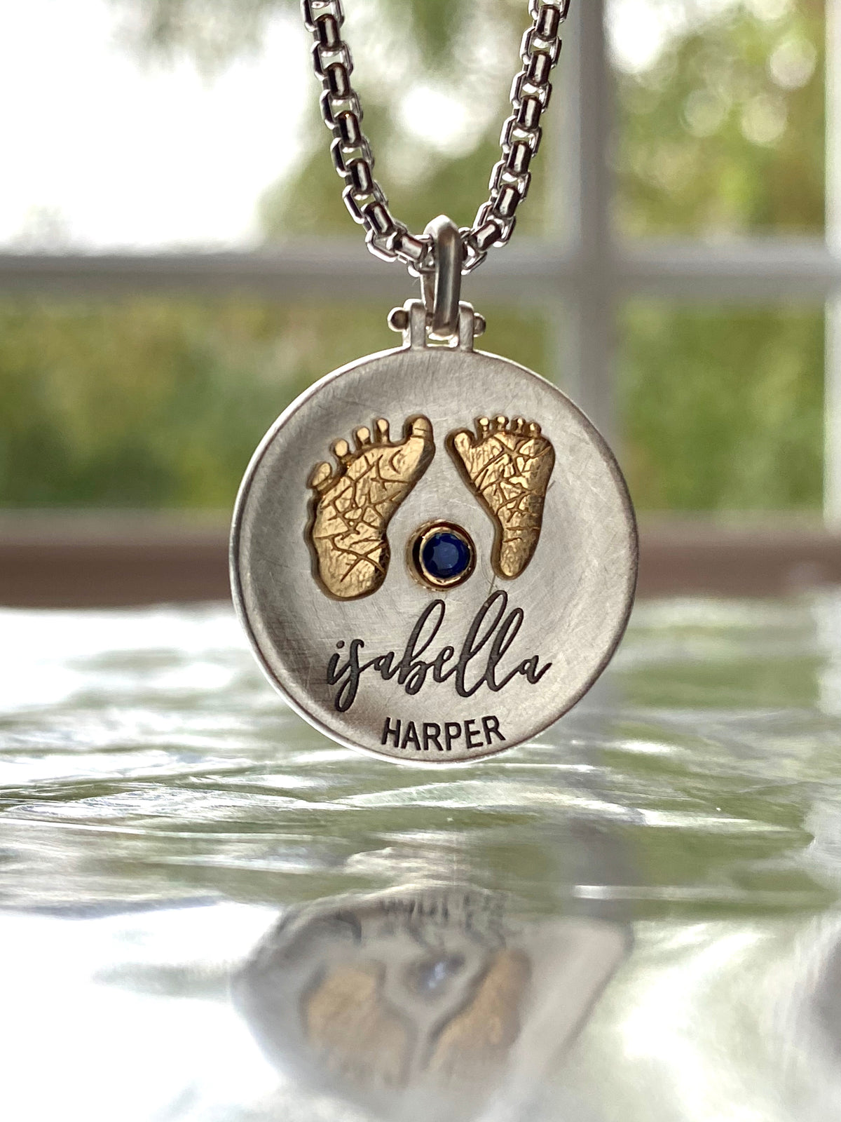 Custom sterling silver pendant with 18K gold baby footprints, a blue sapphire and Isabella lettering