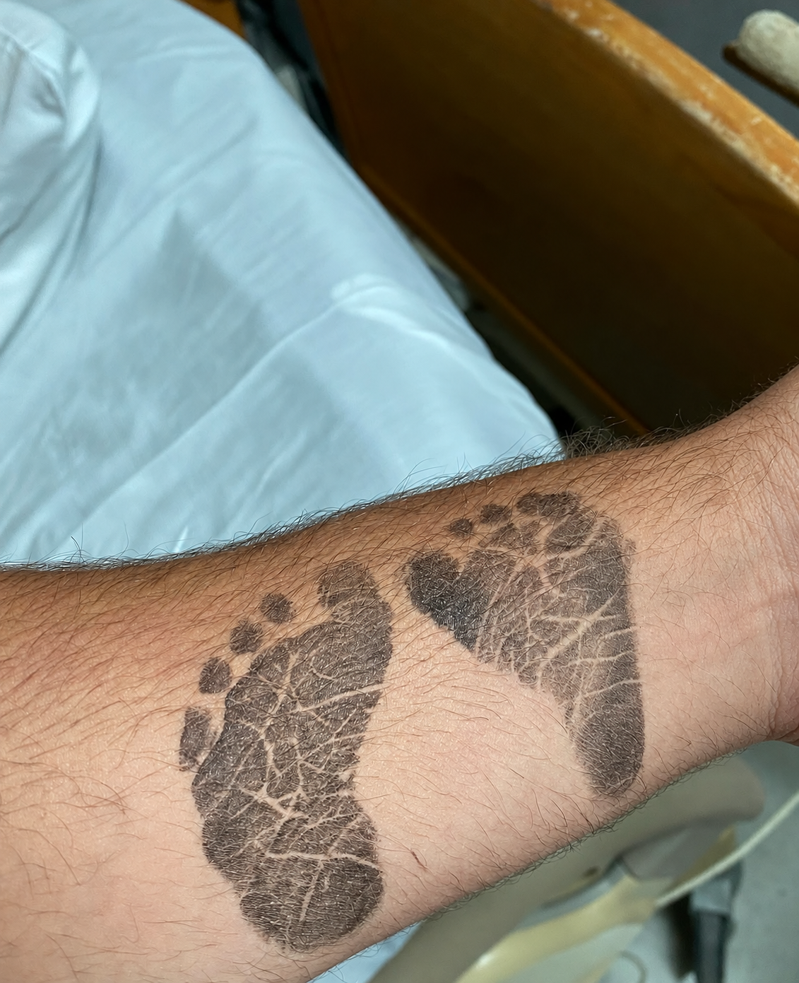 Newborn ink footprints on the father’s forearm, used as the reference for the gold footprints