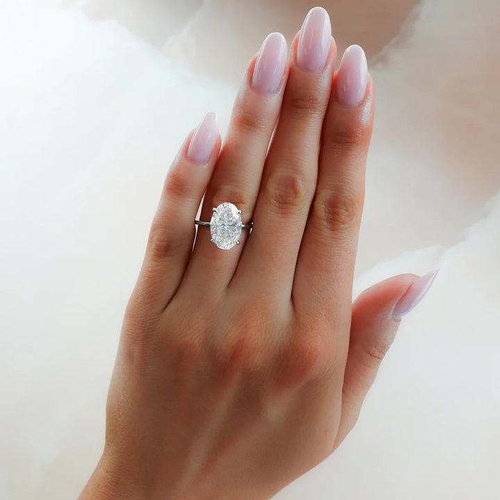 Woman wearing 2.50 carat elongated oval lab diamond engagement ring on finger to show size and scale, 14k yellow gold thin band