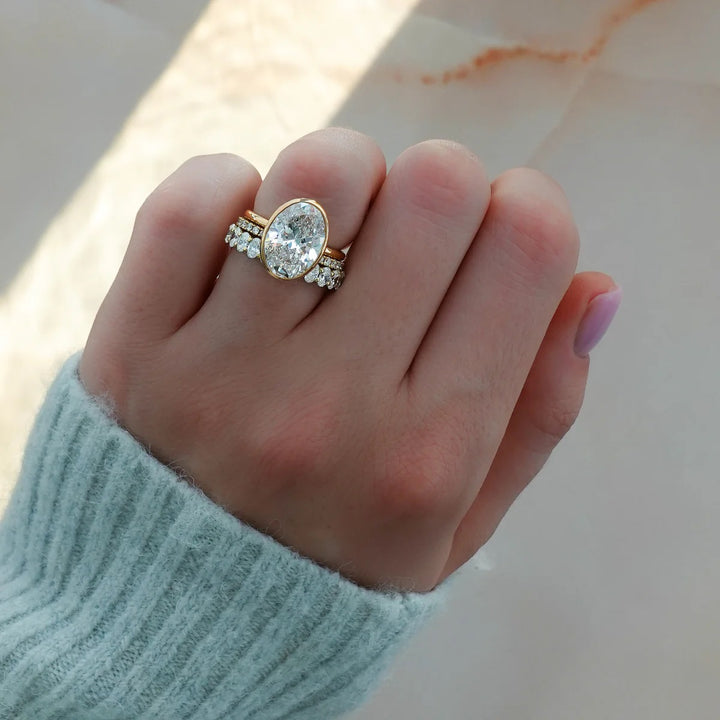 Oval bezel engagement ring stacked perfectly with diamond eternity wedding band, showing flush fit bridal set on hand